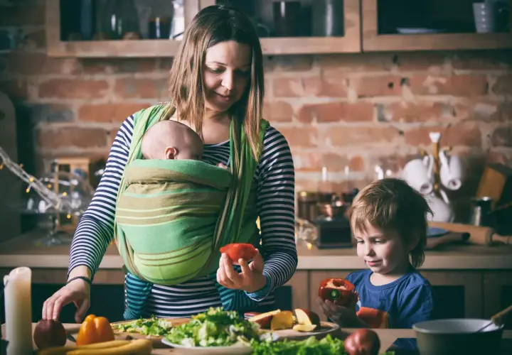 Mama z dzieckiem w chuście i synem przygotowują posiłek. Od kiedy można nosić dziecko w chuście? Od pierwszych dni życia!
