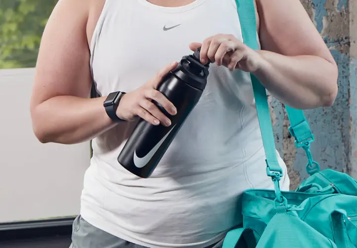 Osoba w białej koszulce sportowej trzyma czarną butelkę Nike. Obok wisi turkusowa torba.