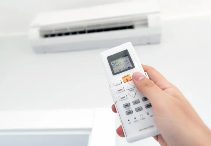 Mano sujetando un control remoto de aire acondicionado, ajustando la temperatura para combatir el calor o el frío.
