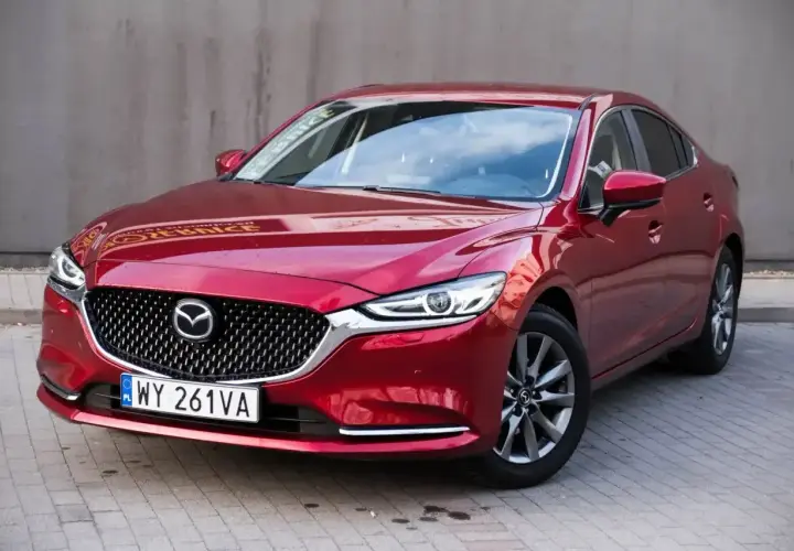 Czerwona Mazda 6 2.0 benzyna z polskimi tablicami rejestracyjnymi stoi na chodniku.