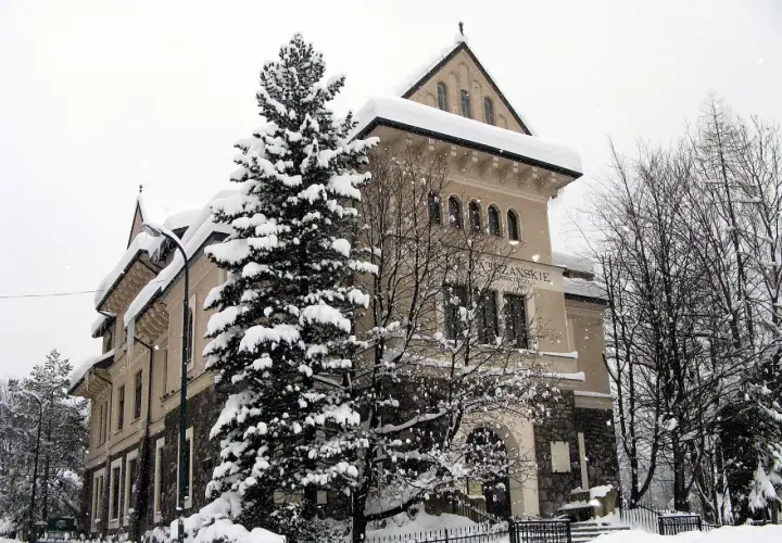 Zimowy dzień w muzeum Tatrzańskiego Parku Narodowego. Śnieg otula drzewa i budynek, tworząc bajkową scenerię.