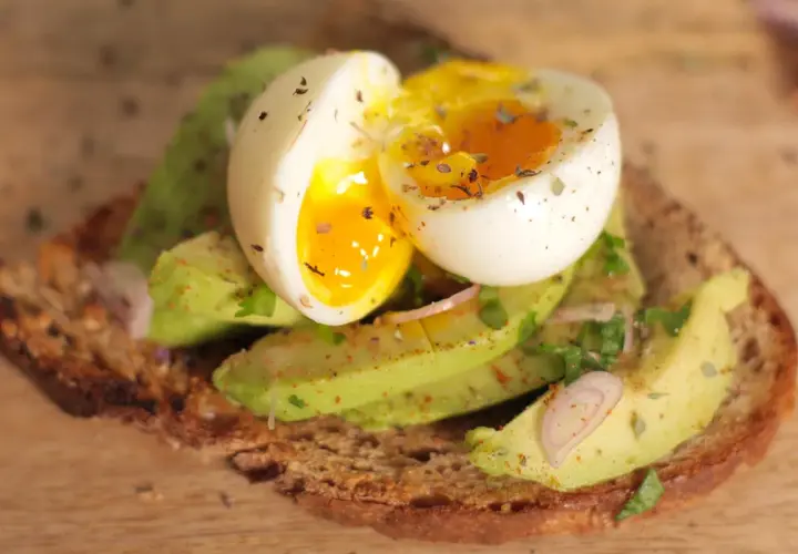 Tartine oeuf et avocat, un délice crémeux avec un jaune coulant, garnie d'herbes fraîches et d'épices sur du pain grillé.