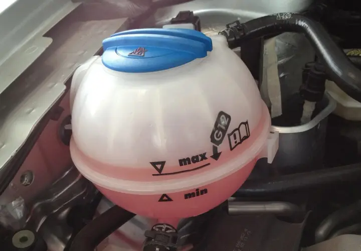 Depósito de refrigerante con líquido rosa. Indica que agua se le echa al coche, entre los niveles "min" y "max", y especifica el tipo G12.