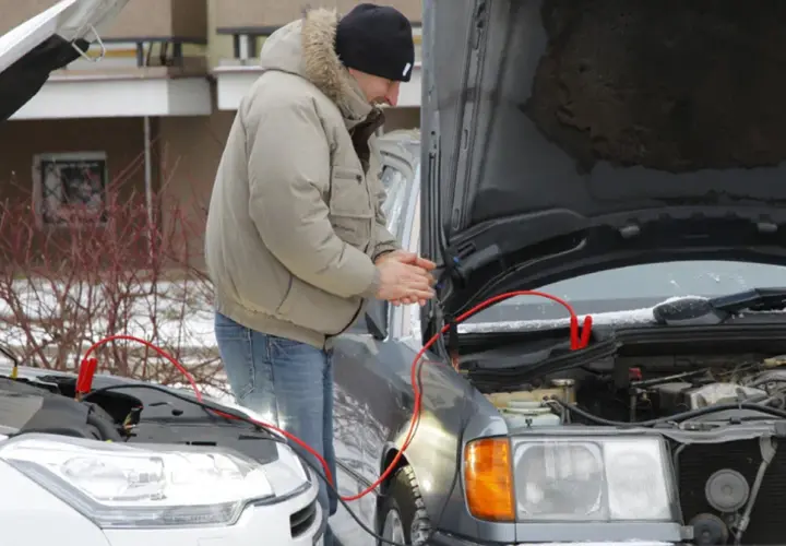 Mężczyzna próbuje odpalić auto zepsutym rozrusznikiem, używając kabli rozruchowych.