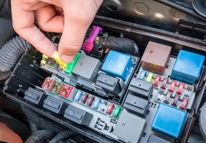 Mano retirando un fusible amarillo de la caja de fusibles del coche. Averiguar cuanto cuesta cambiar un fusible del coche es fácil con esta imagen.