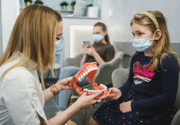 Ortodonta wyjaśnia dziecku budowę szczęki na modelu. W poczekalni siedzą inne osoby.