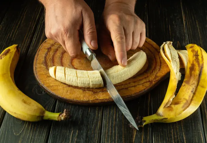 Dłonie kroją banana na desce. To świetny pomysł, co jeść na skurcze nóg, bo banany są bogate w potas.