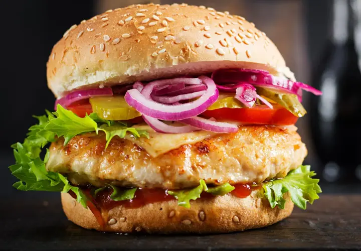 Makro zbliżenie na soczystego burgera drwala: grillowany kotlet, ser, sałata, pomidor, ogórek, czerwona cebula i sos na sezamowej bułce.
