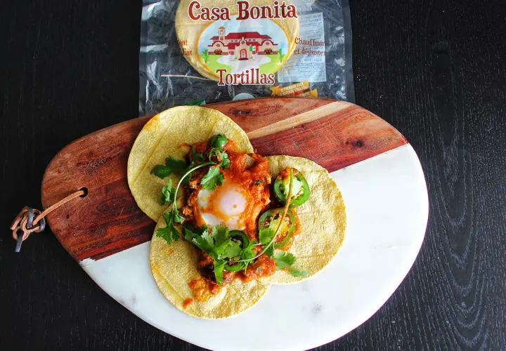 Délicieux huevos rancheros recette sur tortillas, garni d'un œuf coulant, sauce tomate épicée, jalapeños et coriandre fraîche.