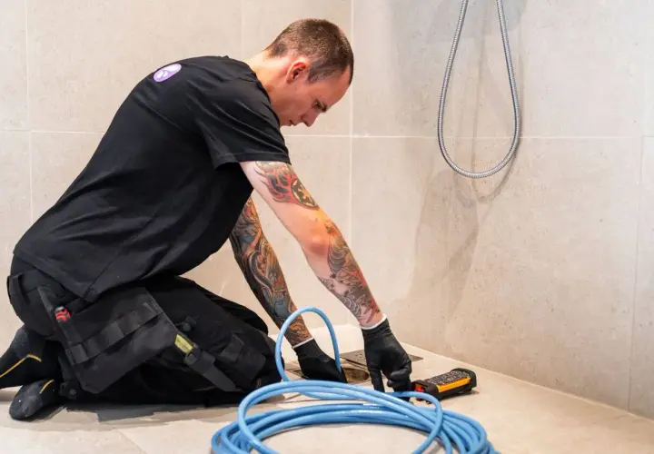 En rörmokare med tatueringar arbetar med en spolbil. Kostnad för spolbil kan variera beroende på problem.