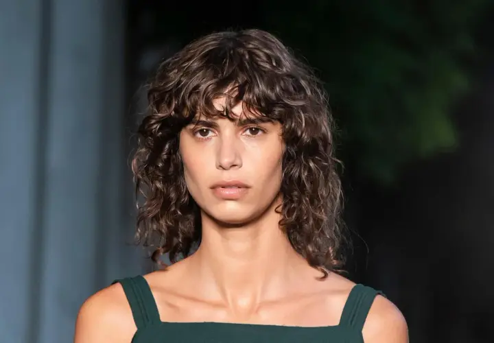 Modelo con cabello castaño ondulado y flequillo rizado, luciendo un vestido verde oscuro.