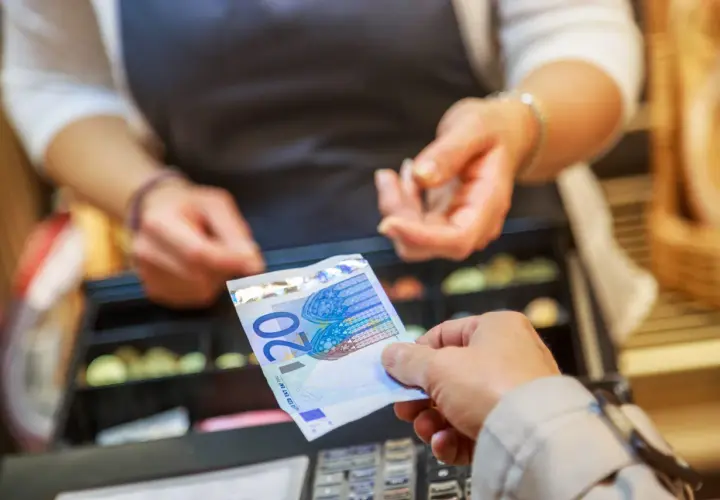 Une main tend un billet de 20 euros pour une saisie avoir espèces. Une caisse enregistreuse est visible en arrière-plan.