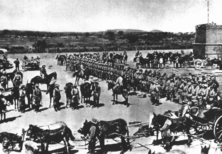 Soldaten und Pferde versammeln sich vor einem Turm. Die Szene erinnert an die Schlacht am Waterberg, ein entscheidendes Ereignis in der Kolonialgeschichte.
