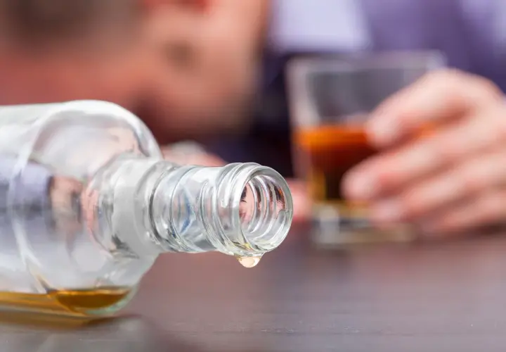 Objawy zafałszowania alkoholu: jak rozpoznać metanol w domowej wódce? Kropla alkoholu z butelki, w tle osoba z kieliszkiem.