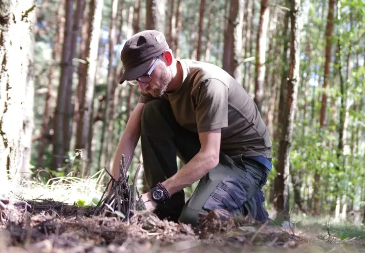 Mężczyzna w lesie przygotowuje rozpałkę do ogniska. To przykład, jak radzić sobie w trudnych warunkach, czyli survival co to znaczy w praktyce.