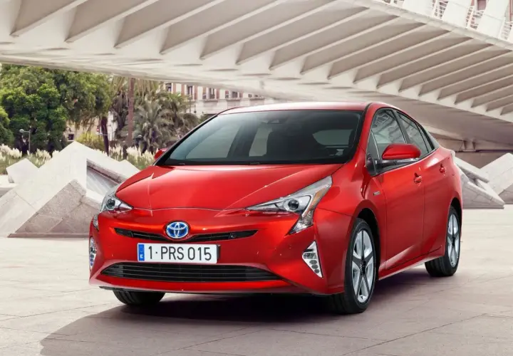 Czerwony Prius 4 z nowoczesnym designem, zaparkowany pod betonową konstrukcją z palmami w tle.