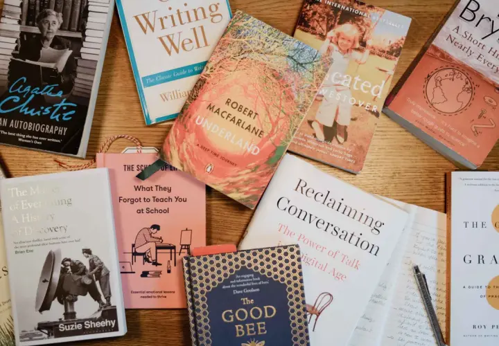 Une pile de livres sur une table en bois, parfaite pour un podcast littéraire. On y trouve des biographies, des essais et des romans.