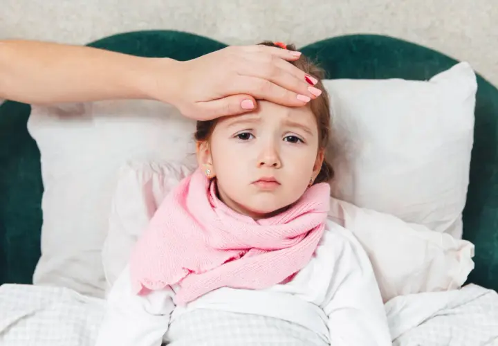 Bambina a letto con sciarpa rosa, mano sulla fronte per controllare la febbre, forse la quarta malattia.