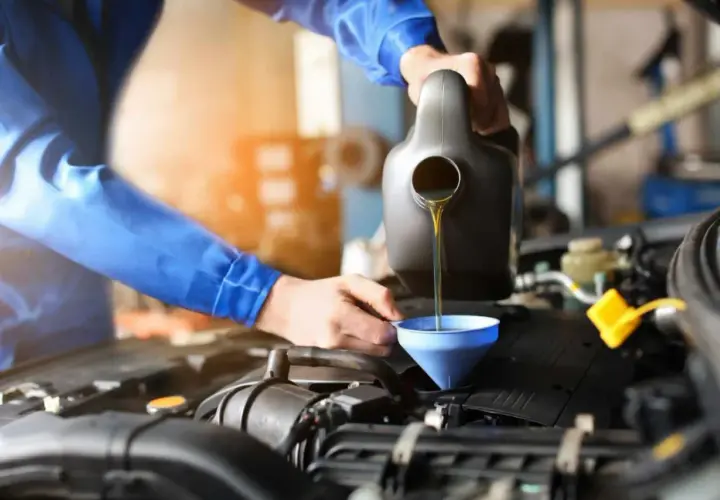 Mechanik w niebieskim kombinezonie wykonuje wymianę oleju w samochodzie, nalewając płyn do silnika przez lejek.
