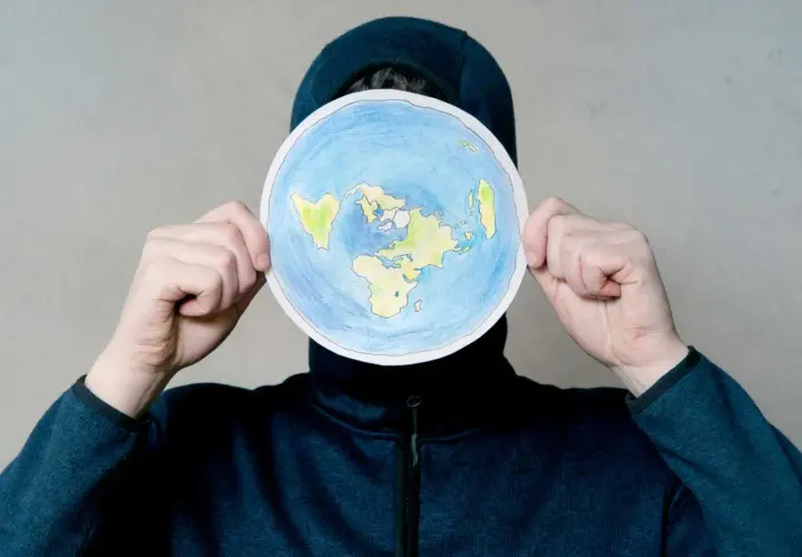 Osoba w kapturze trzyma okrągły rysunek płaskiej Ziemi. To nie jest globe po polsku, ale ciekawa wizja świata.