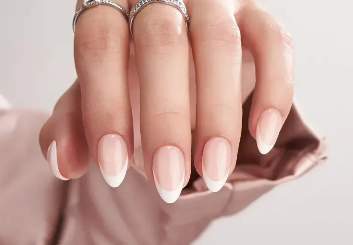 En hand med eleganta, korta french naglar och två glittrande ringar.