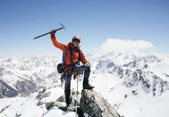 Szczęśliwy alpinista na szczycie, z lodowym toporem w dłoni, podziwia majestatyczne szczyty górskie.