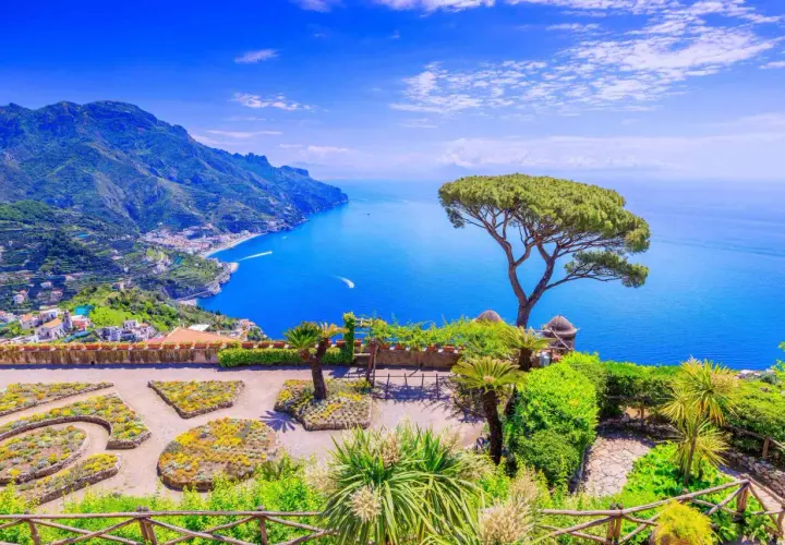 A stunning view of the Amalfi Coast, a perfect destination for a trip from Naples. Lush gardens overlook the sparkling blue sea and dramatic cliffs.