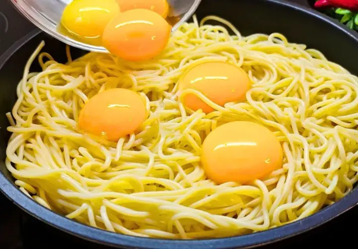Makaron z jajkiem w patelni, żółtka tworzą złote kropki na żółtym tle.