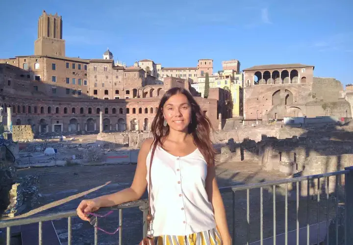 A woman smiles in front of ancient Roman ruins, enjoying a sunny day. This scene suggests that Rome is safe and welcoming for tourists.