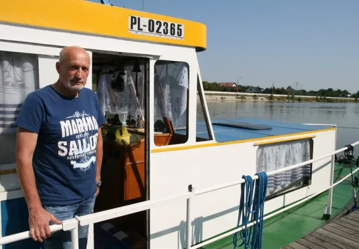 Mężczyzna na pokładzie statku, symbolizującego transport rzeczny. Widoczna tablica rejestracyjna PL-02365.