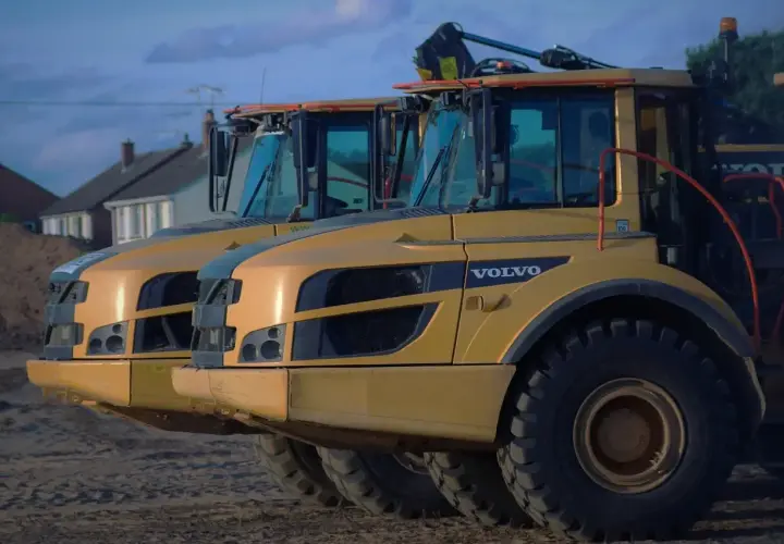 Dwa żółte wywrotki Volvo A30D stoją obok siebie. W tle domy i niebo.