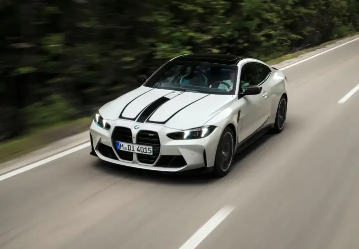 Białe BMW F82 z czarnymi pasami na masce pędzi po krętej drodze wśród zieleni.