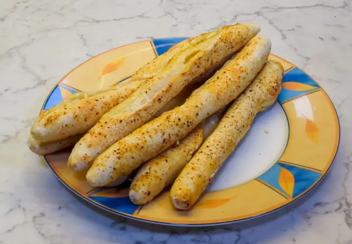 Leckere, knusprige brotstangen aus pizzateig, bestreut mit Gewürzen, liegen auf einem bunten Teller.
