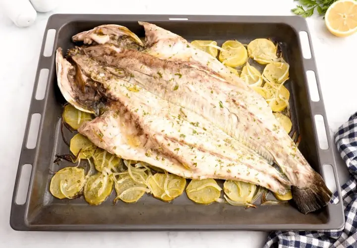 Corvina entera asada con patatas y limón en una bandeja. Una deliciosa opción para tus recetas de corvina.