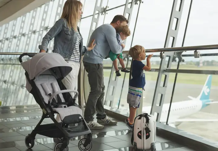 Famiglia in aeroporto, con passeggino e valigia, guarda un aereo. Speriamo che i bambini non soffrano di mal d'aereo!