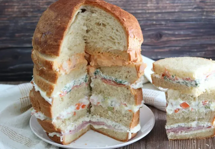 Un monumentale pane gastronomico a più strati, farcito con salmone, verdure e salse cremose, accanto a una versione più piccola.