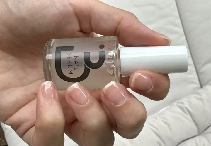 En hand håller en flaska nagelserum. Naglarna ser naturligt starkare och glansiga ut.