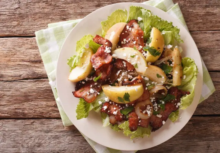 Une délicieuse idée de salade composée : lard croustillant, pommes de terre rôties, oignons caramélisés et fromage émietté sur un lit de laitue.