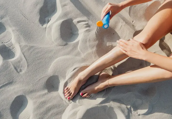 Kobieta smaruje nogi kremem z filtrem zawierającym ethylhexyl methoxycinnamate na piaszczystej plaży.