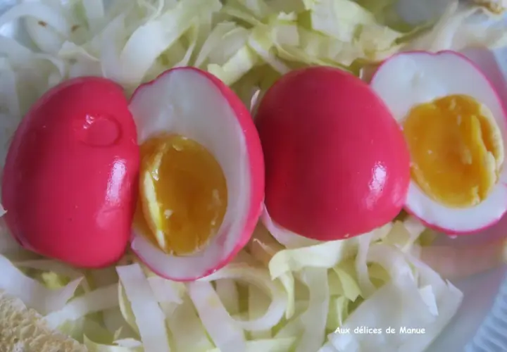 Trois œufs durs à la coquille rose vif, dont deux coupés révèlent un jaune d'œuf coulant, servis sur un lit de chou blanc émincé.