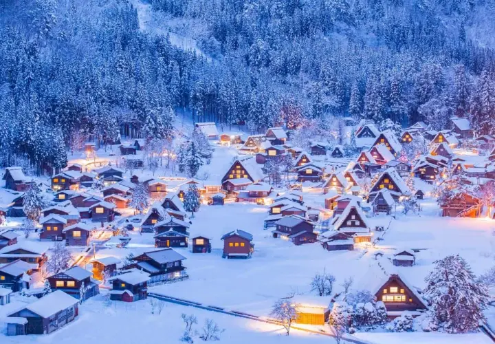 Ein verschneites Dorf in Japan im Winter. Traditionelle Häuser mit warmem Licht sind von schneebedeckten Bäumen umgeben.