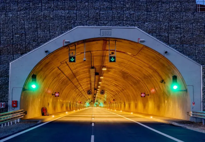 Wjazd do tunelu z kamienną górą w tle. Zielone światła sygnalizacyjne i znaki ograniczenia prędkości 80 km/h.