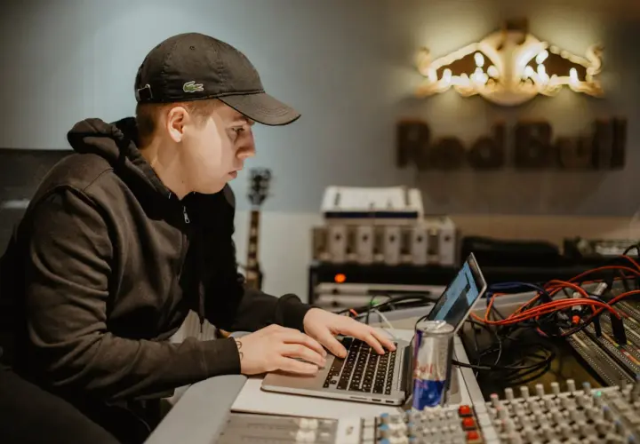 Un jeune beatmaker français concentré sur son ordinateur portable dans un studio d'enregistrement, une canette Red Bull à portée de main.