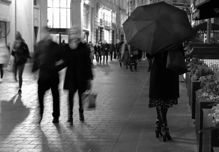 Nocne street photography. Rozmyte postacie spieszą się ulicą, jedna osoba z parasolką.
