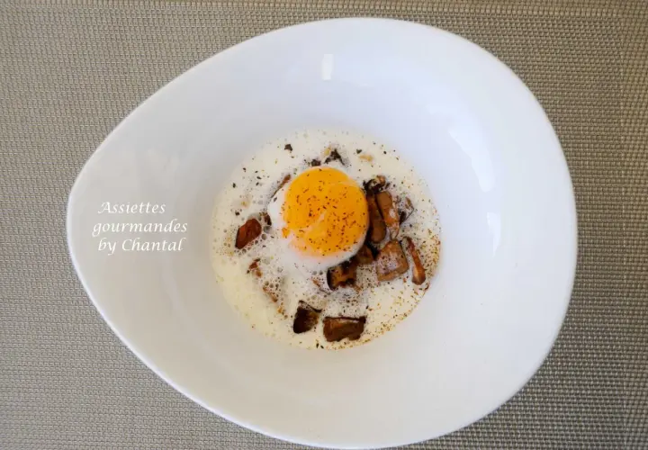 Un œuf poché, entouré de morceaux de champignons et d'une mousse légère, dans une assiette blanche. Des oeufs parfaits pour un repas gourmand.