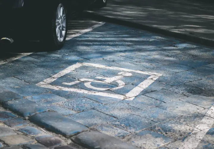Wyznaczone miejsce parkingowe dla niepełnosprawnych pod blokiem. Symbol wózka inwalidzkiego na niebieskim tle.