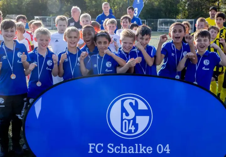 Junge Fußballer der Schalke U10 jubeln mit Medaillen vor einem Banner des FC Schalke 04.