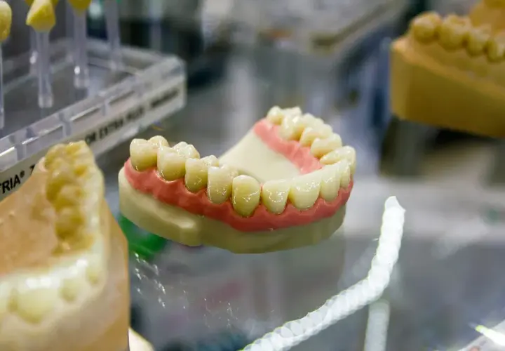 Modello di dentiera mobile con denti bianchi e gengive rosa su un piano di vetro.