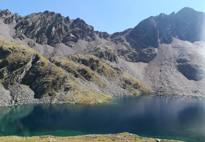 Lago sereno y montañas rocosas cerca del refugi de Baiau.