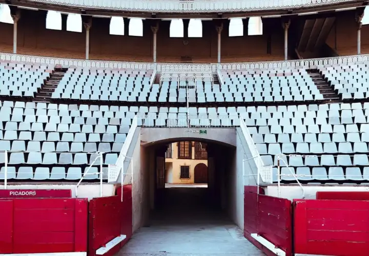Vista de la plaza de toros vacía, con filas de asientos blancos y la contrabarrera roja.